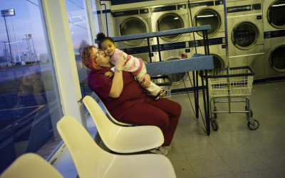 Mother with her child at the laundromat, out of downtown in a strip mall close to the interstate highway.